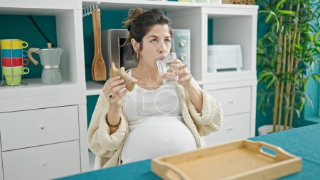 Foto de Joven embarazada comiendo sándwich bebiendo agua en el comedor - Imagen libre de derechos