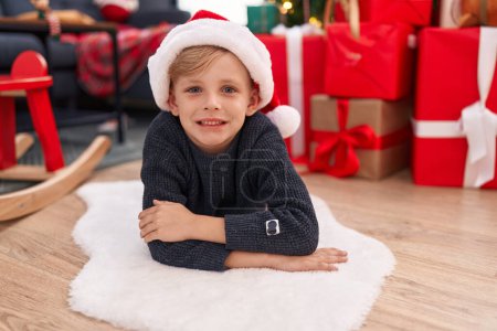 Foto de Adorable niño sonriendo confiado mintiendo por el árbol de Navidad en casa - Imagen libre de derechos
