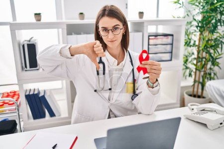 Photo for Young caucasian doctor woman holding support red ribbon with angry face, negative sign showing dislike with thumbs down, rejection concept - Royalty Free Image