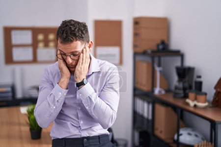 Foto de Joven hombre hispano en la oficina con expresión triste cubriendo la cara con las manos mientras llora. concepto de depresión. - Imagen libre de derechos