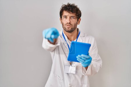 Photo for Hispanic scientist man working with tablet pointing with finger to the camera and to you, confident gesture looking serious - Royalty Free Image