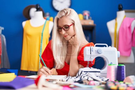 Téléchargez les photos : Jeune femme blonde tailleur souriant dessin confiant sur ordinateur portable au studio de couture - en image libre de droit
