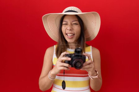 Téléchargez les photos : Femme chinoise du Moyen Age utilisant un appareil photo réflexe portant un chapeau d'été en colère et fou hurlant frustré et furieux, criant de colère. rage et concept agressif. - en image libre de droit