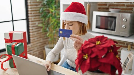 Foto de Joven rubia de compras con portátil y tarjeta de crédito celebrando la Navidad en el comedor - Imagen libre de derechos
