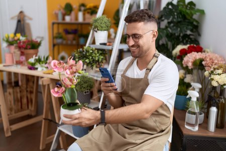 Foto de Floristería joven hombre hispano hacer foto para plantar por teléfono inteligente en la tienda de flores - Imagen libre de derechos