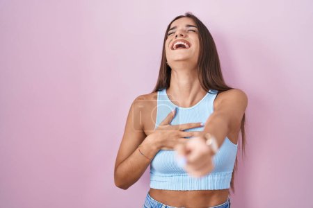 Téléchargez les photos : Jeune femme brune debout sur fond rose se moquant de vous, pointant du doigt la caméra avec la main sur le corps, expression de honte - en image libre de droit