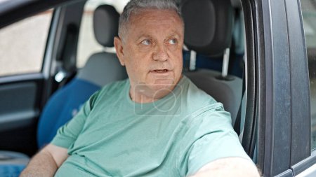 Téléchargez les photos : Homme aux cheveux gris d'âge moyen assis en voiture dans la rue - en image libre de droit