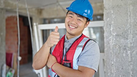 Téléchargez les photos : Constructeur souriant confiant faire pouce vers le haut geste sur le chantier de construction - en image libre de droit