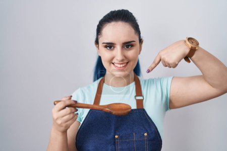 Photo for Young modern girl with blue hair wearing cook apron holding spoon pointing finger to one self smiling happy and proud - Royalty Free Image