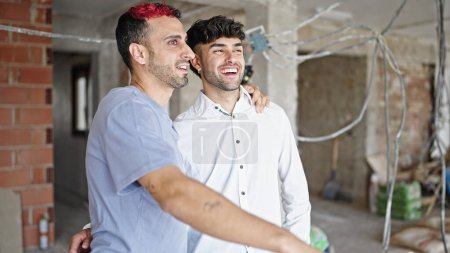 Foto de Dos hombres se abrazan mirando a su alrededor en el sitio de construcción - Imagen libre de derechos