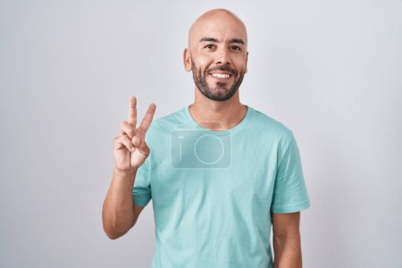 Foto de Hombre calvo de mediana edad parado sobre fondo blanco mostrando y señalando hacia arriba con los dedos número dos mientras sonríe confiado y feliz. - Imagen libre de derechos