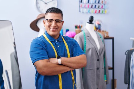 Téléchargez les photos : Jeune homme latino tailleur souriant confiant debout avec les bras croisés geste à l'atelier - en image libre de droit