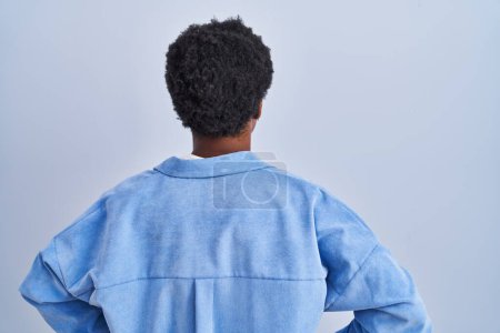 Foto de Mujer afroamericana de pie sobre fondo azul de pie hacia atrás mirando hacia otro lado con los brazos en el cuerpo - Imagen libre de derechos