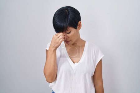 Photo for Young asian woman with short hair standing over isolated background tired rubbing nose and eyes feeling fatigue and headache. stress and frustration concept. - Royalty Free Image