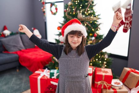 Photo for Adorable hispanic girl unpacking gift sitting by christmas tree at home - Royalty Free Image