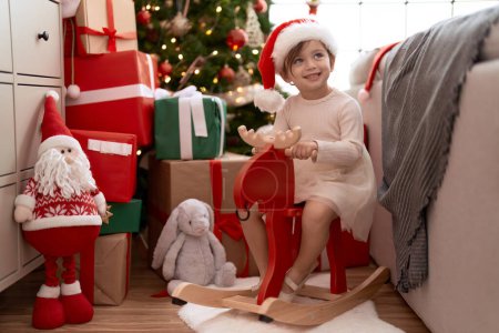 Téléchargez les photos : Adorable fille assise sur renne à bascule par arbre de Noël à la maison - en image libre de droit