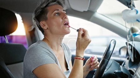 Téléchargez les photos : Jeune femme assise sur la voiture maquillage lèvres à la rue - en image libre de droit
