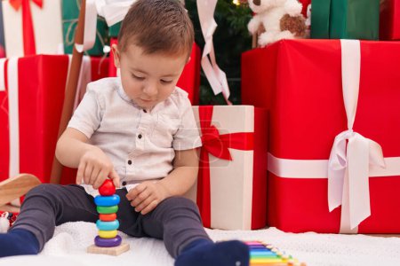 Photo for Adorable hispanic toddler playing with toys sitting on floor by christmas gifts at home - Royalty Free Image
