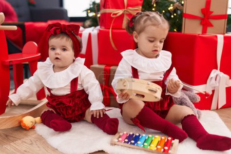 Foto de Adorables chicas jugando xilófono y pandereta celebrando la Navidad en casa - Imagen libre de derechos