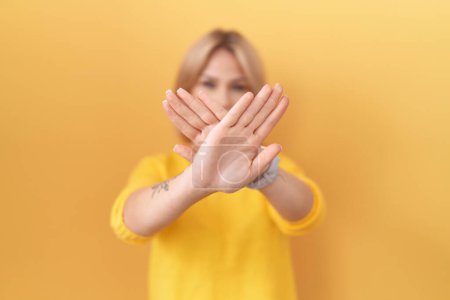 Foto de Mujer joven caucásica usando expresión de rechazo suéter amarillo cruzando brazos y palmas haciendo signo negativo, cara enojada - Imagen libre de derechos