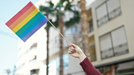 Foto de Joven hispano sosteniendo bandera de arco iris en la calle - Imagen libre de derechos