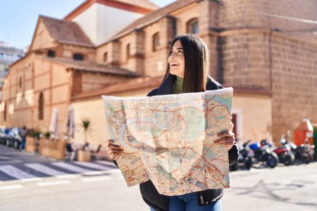 Téléchargez les photos : Jeune belle femme hispanique souriant confiant tenant la carte de la ville à la rue - en image libre de droit
