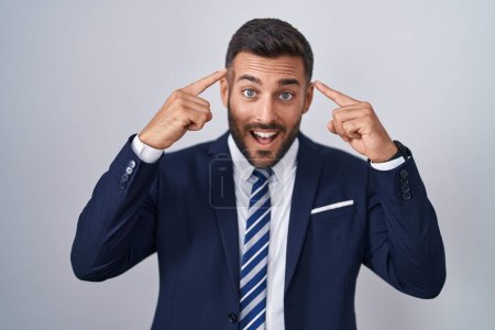 Photo for Handsome hispanic man wearing suit and tie smiling pointing to head with both hands finger, great idea or thought, good memory - Royalty Free Image