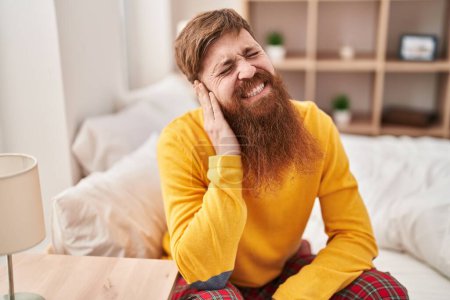 Téléchargez les photos : Young redhead man suffering for ear pain sitting on bed at bedroom - en image libre de droit