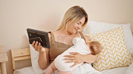 Photo for Mother and daughter sitting on bed breastfeeding baby looking photo at bedroom - Royalty Free Image