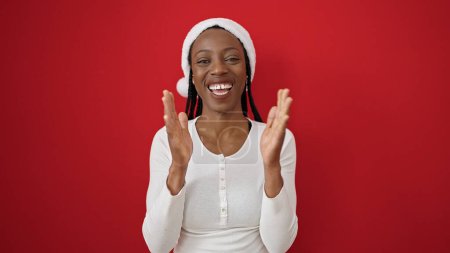 Photo for African american woman wearing christmas hat clapping hands over isolated red background - Royalty Free Image