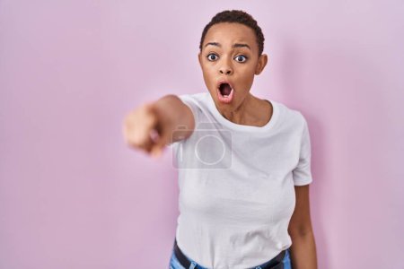 Photo for Beautiful african american woman standing over pink background pointing with finger surprised ahead, open mouth amazed expression, something on the front - Royalty Free Image