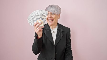 Foto de Mujer joven sosteniendo dólares sonriendo sobre fondo rosa aislado - Imagen libre de derechos