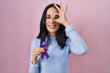 Téléchargez les photos : Femme hispanique tenant un ruban violet conscience souriant heureux faire ok signe avec la main sur les yeux en regardant à travers les doigts - en image libre de droit