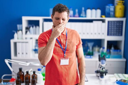 Foto de Hombre hispano joven que trabaja en el laboratorio científico sintiéndose mal y tosiendo como síntoma de resfriado o bronquitis. concepto de atención sanitaria. - Imagen libre de derechos