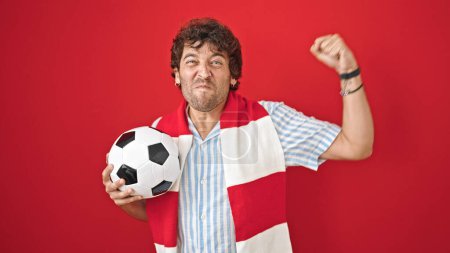 Téléchargez les photos : Jeune homme hispanique soutenant l'équipe de football célébrant sur fond rouge isolé - en image libre de droit