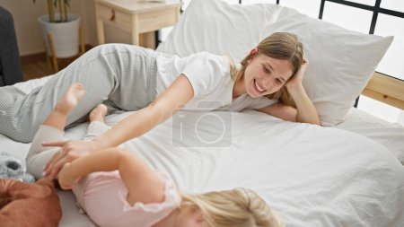 Téléchargez les photos : Bonne mère caucasienne et petite fille, confortablement couchée sur le lit et souriante, profitant d'une matinée de détente ensemble dans une chambre confortable à la maison - en image libre de droit