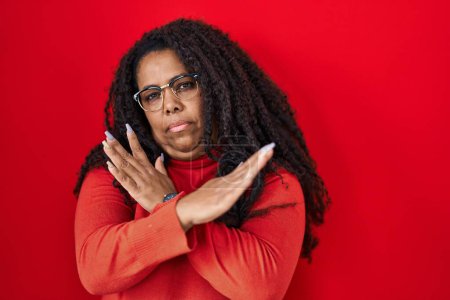 Foto de Más tamaño mujer hispana de pie sobre fondo rojo expresión de rechazo cruzando brazos haciendo signo negativo, cara enojada - Imagen libre de derechos