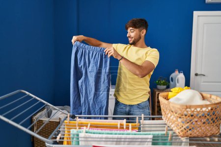 Téléchargez les photos : Young arab man smiling confident hanging clothes on clothesline at laundry room - en image libre de droit