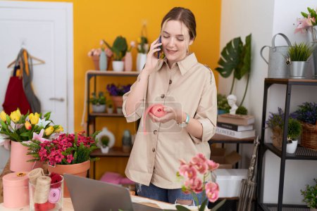 Téléchargez les photos : Jeune fleuriste femme caucasienne parlant sur smartphone tenant dentelle cadeau à la boutique de fleurs - en image libre de droit
