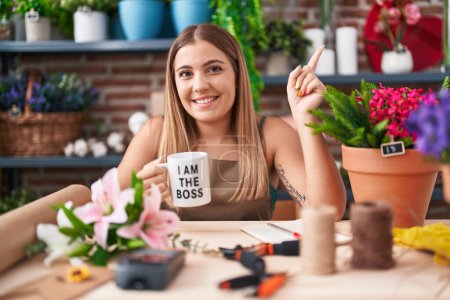 Photo for Young blonde woman working at florist shop holding i am the boss cup smiling happy pointing with hand and finger to the side - Royalty Free Image