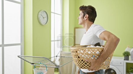 Photo for Young hispanic man holding basket with clothes looking upset at laundry room - Royalty Free Image