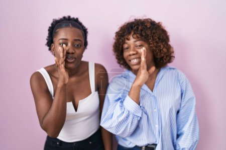Photo for Two african women standing over pink background hand on mouth telling secret rumor, whispering malicious talk conversation - Royalty Free Image