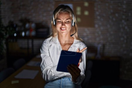 Téléchargez les photos : Jeune femme blonde travaillant au bureau la nuit pointant de côté inquiet et nerveux avec l'index, préoccupé et expression surprise - en image libre de droit