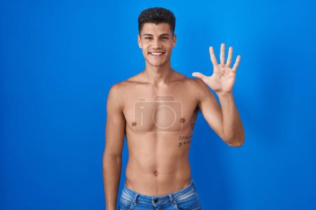 Photo for Young hispanic man standing shirtless over blue background showing and pointing up with fingers number five while smiling confident and happy. - Royalty Free Image