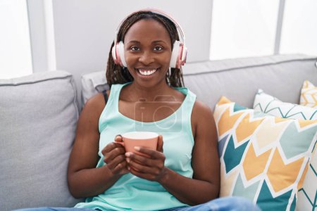 Téléchargez les photos : Femme afro-américaine écoutant de la musique boire du café à la maison - en image libre de droit
