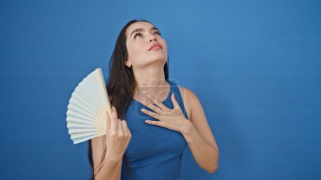 Foto de Mujer hispana hermosa joven usando ventilador de mano sudando sobre fondo azul aislado - Imagen libre de derechos
