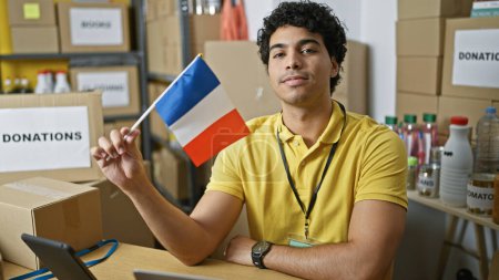 Téléchargez les photos : Jeune homme latin bénévole tenant le drapeau français au centre de charité - en image libre de droit