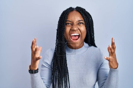 Photo for African american woman standing over blue background crazy and mad shouting and yelling with aggressive expression and arms raised. frustration concept. - Royalty Free Image