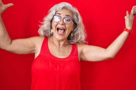 Photo for Middle age woman with grey hair standing over red background celebrating crazy and amazed for success with arms raised and open eyes screaming excited. winner concept - Royalty Free Image