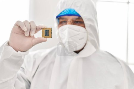 Photo for Young latin man scientist wearing covid protection uniform holding cpu processor chip at laboratory - Royalty Free Image
